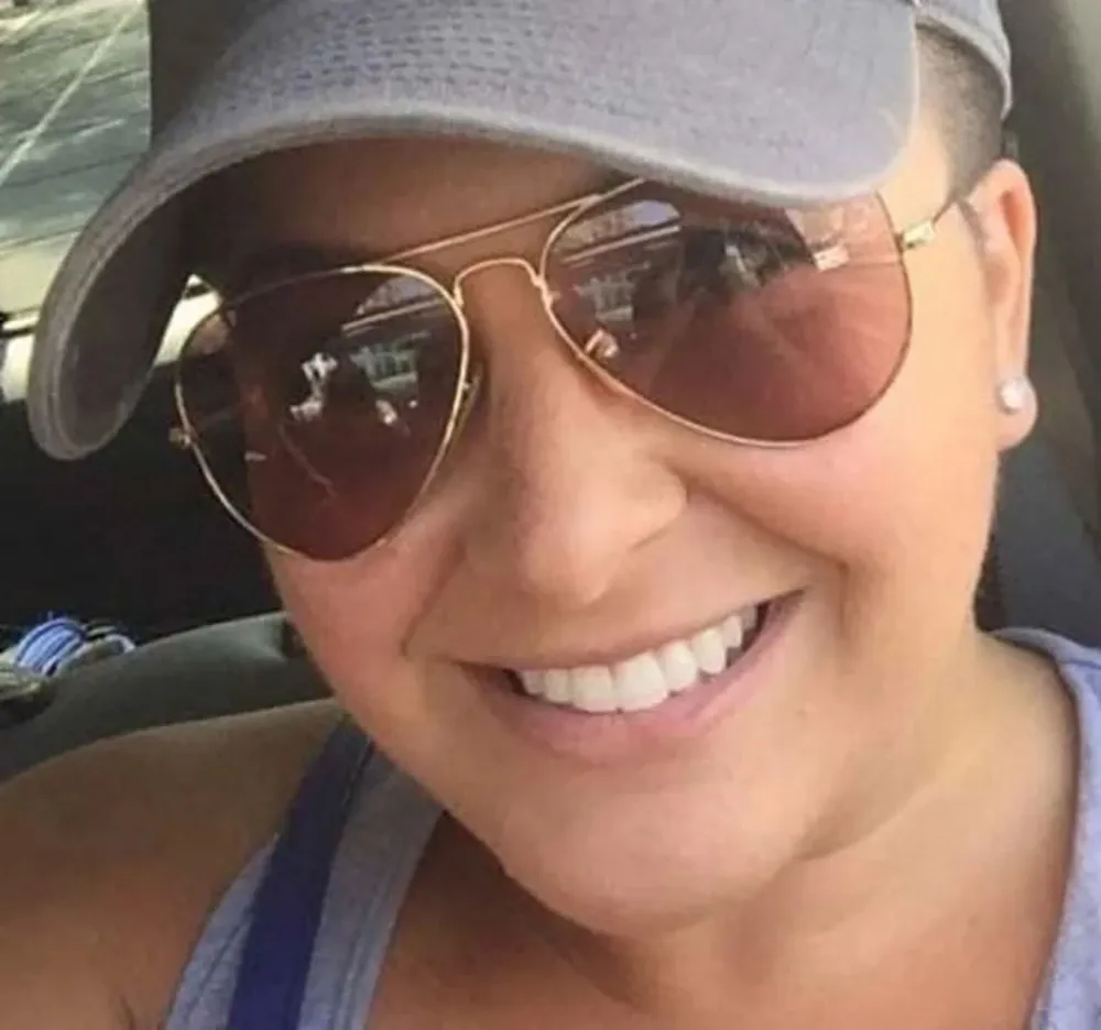 Close-up of Vanessa O'Rourke, wanted for wire fraud, smiling while wearing sunglasses and a baseball cap.