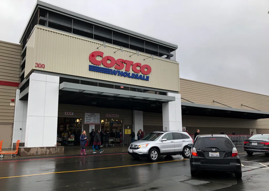 A view of a Costco store with cars and people outside the entrance.