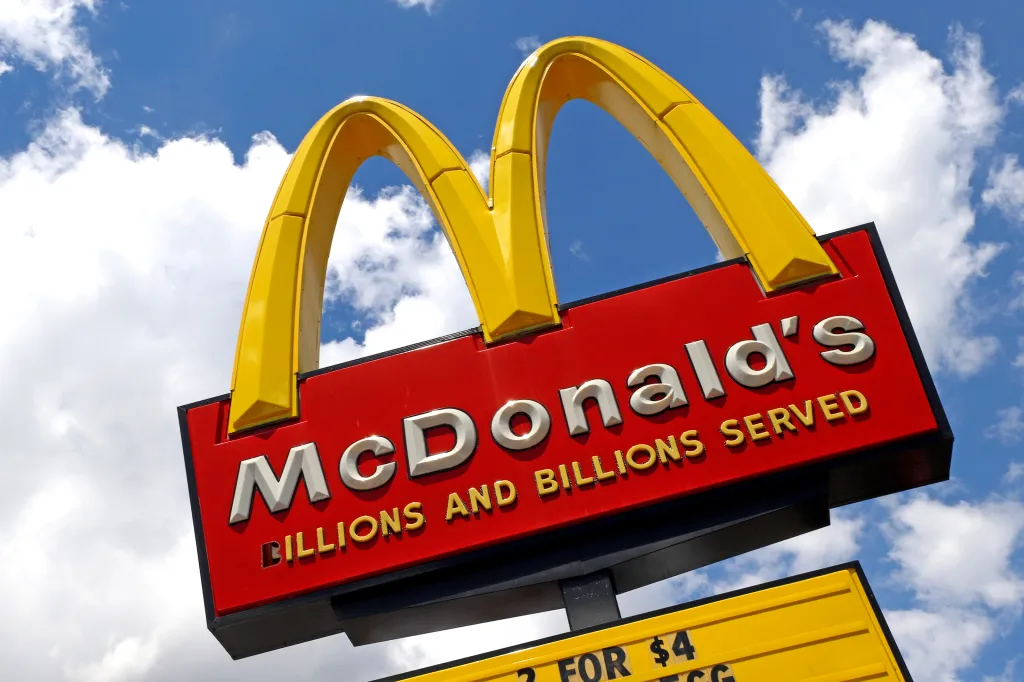McDonald's sign with golden arches against a blue sky with clouds.