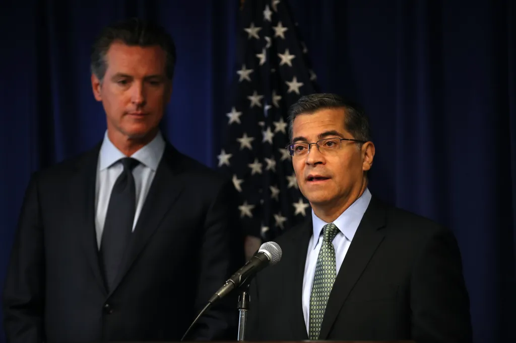 Xavier Becerra speaking at a news conference while Gavin Newsom looks on.