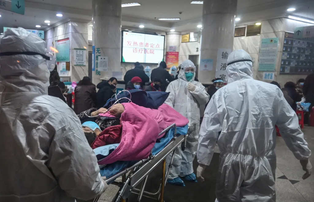 Medical staff in hazmat suits transport a patient on a stretcher through a hospital.