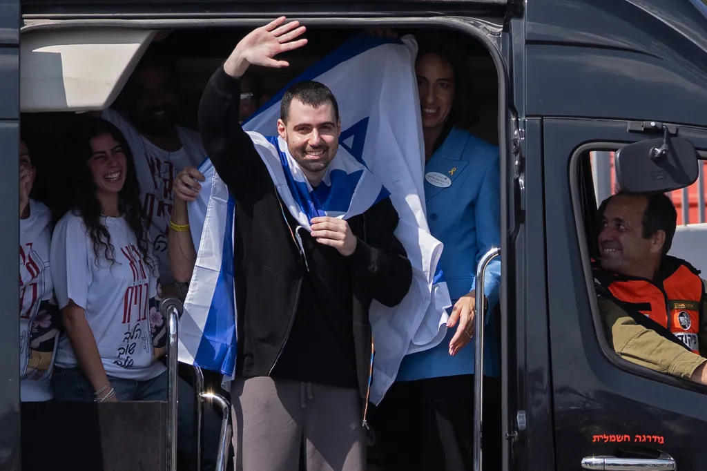 Former hostage Guy Gilboa-Dalal waves to supporters while wrapped in an Israeli flag from inside a vehicle.