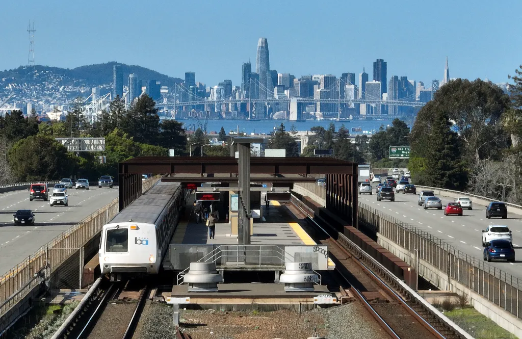 A BART train at the Rockridge station in Oakland, California, with the San Francisco skyline visible in the background.