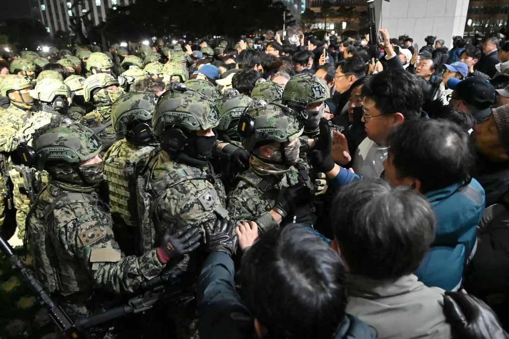 Soldiers in camouflage uniforms and helmets blocking a crowd of people.