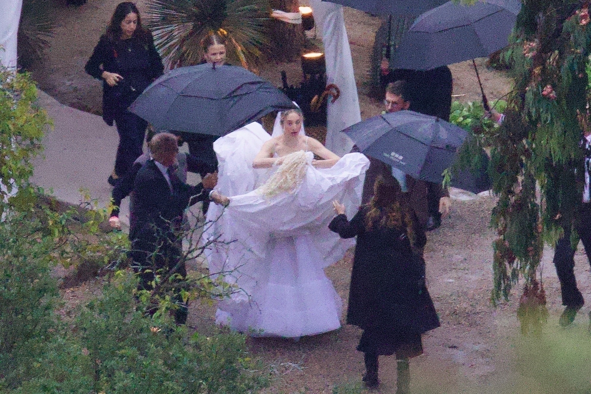 Este Haim being escorted by guests holding umbrellas and her wedding dress at her New Year's Eve wedding in Ojai, California.