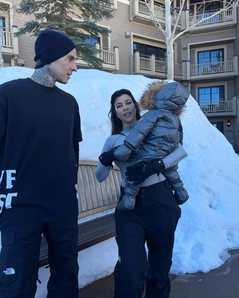 Kourtney Kardashian holding a baby, Roxky, next to Travis Barker on a snowy day.