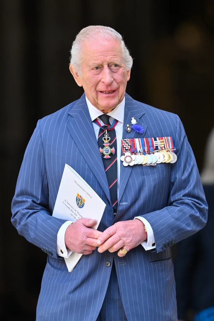 King Charles III wearing a pinstripe suit with medals, holding a program for the VE Day 80th anniversary service.