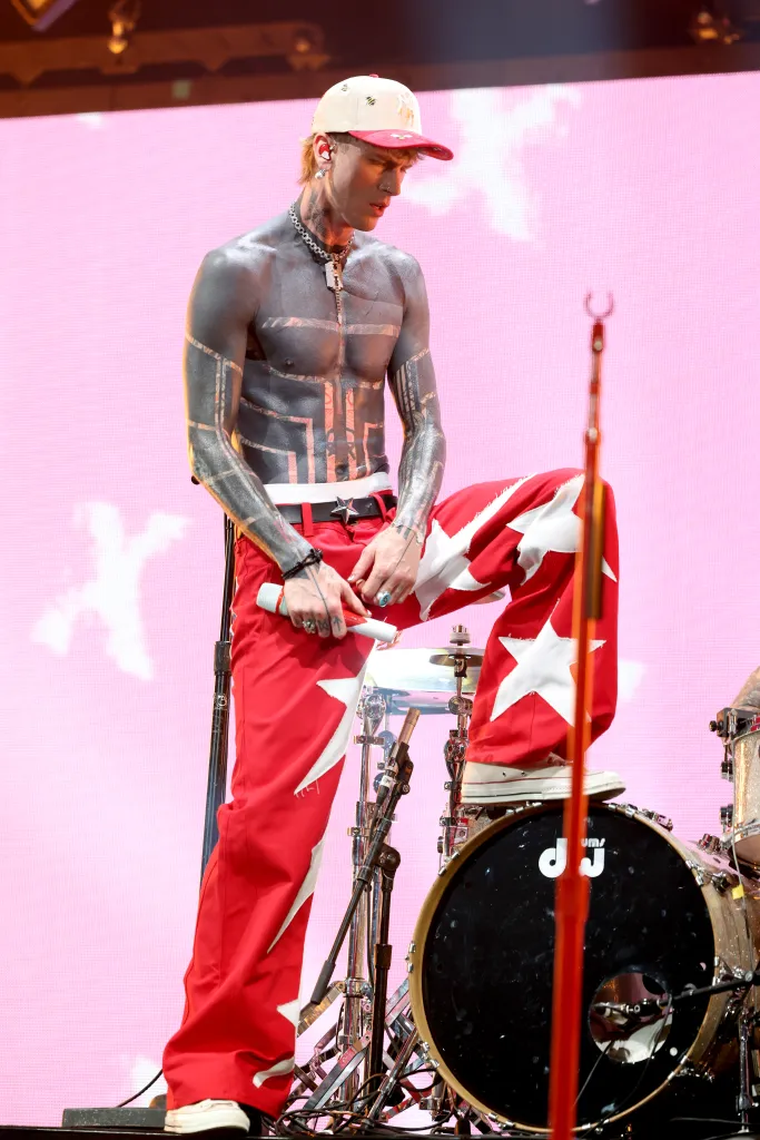 MGK performing in red pants with white stars and a bare chest with black tribal-style tattoos.