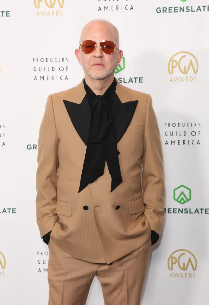 Ryan Murphy attending the Producers Guild Awards in a tan suit with a black bow tie and orange-tinted aviator sunglasses.