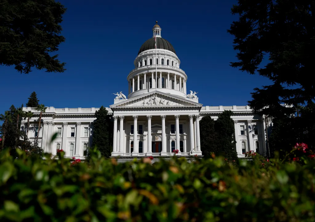 California State Capitol building with a clear blue sky, viewed through green foliage.