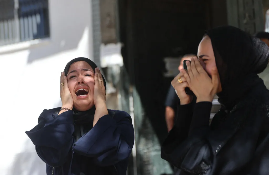A woman with her hands to her face cries out, while another woman holds a phone to her face, during a funeral for a man killed in an Israeli airstrike.