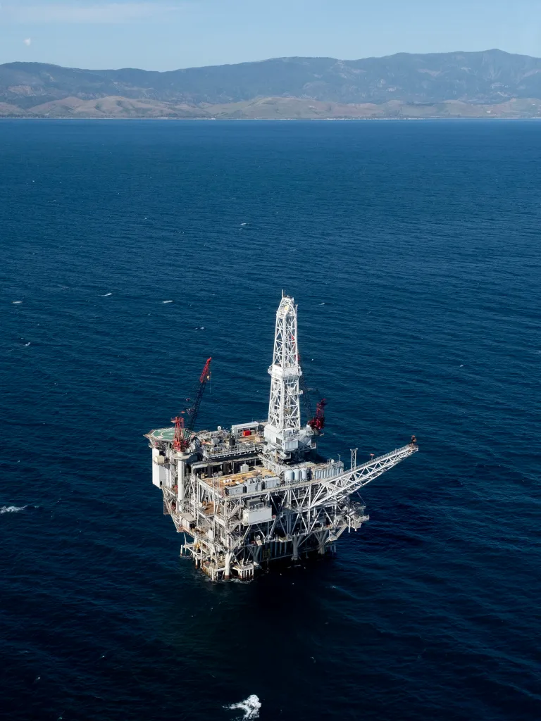 Aerial view of the Harmony Platform oil rig in the ocean with mountains in the background.