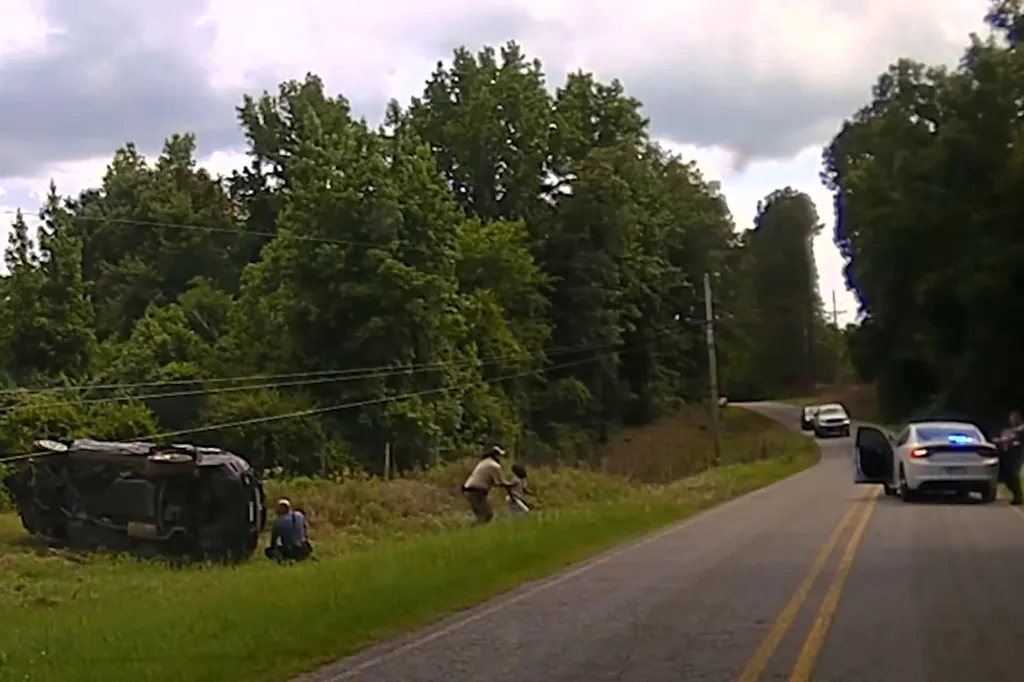 Footage showing an SUV crashed on its side in a ditch while a police officer attends to a child.