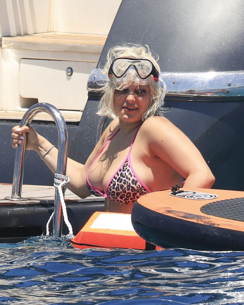 Bebe Rexha in an animal print bikini top and goggles, climbing out of the water onto a boat in Ibiza.