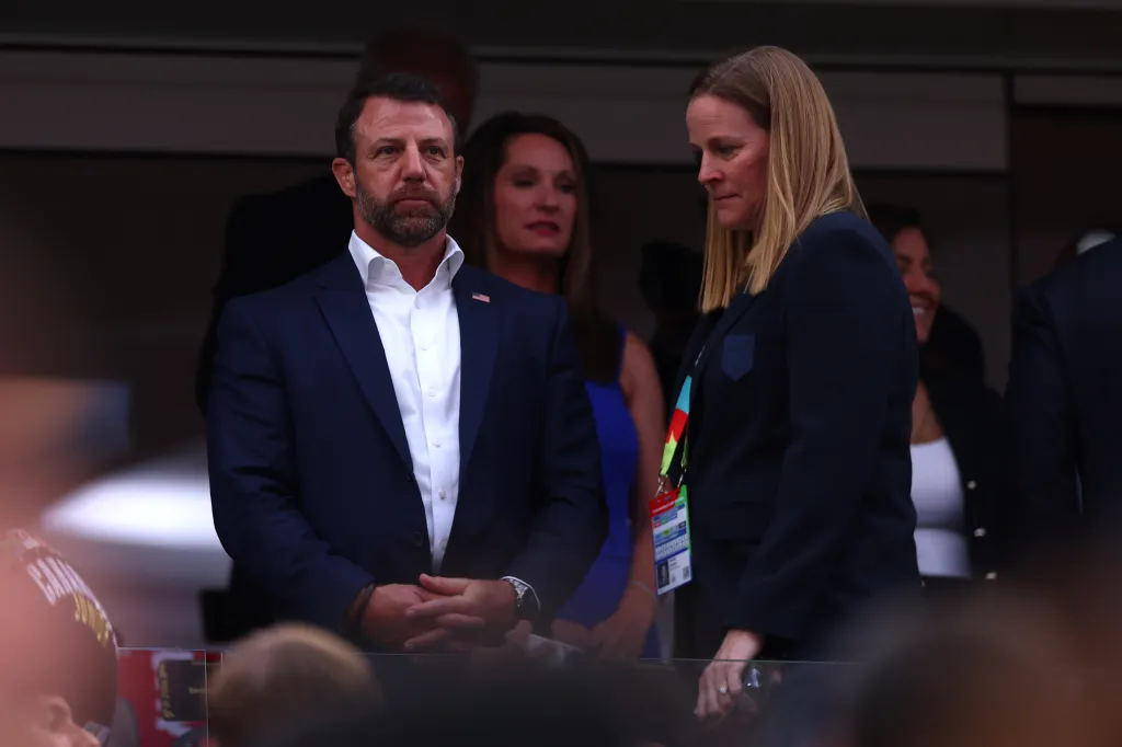 U.S. Secretary of Homeland Security Markwayne Mullin and a woman in a suit observe a soccer match.