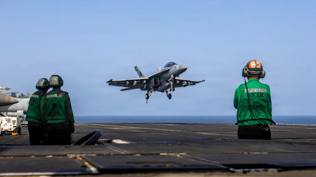 An F/A-18E Super Hornet landing on the USS Abraham Lincoln aircraft carrier, with crew members in green observing.