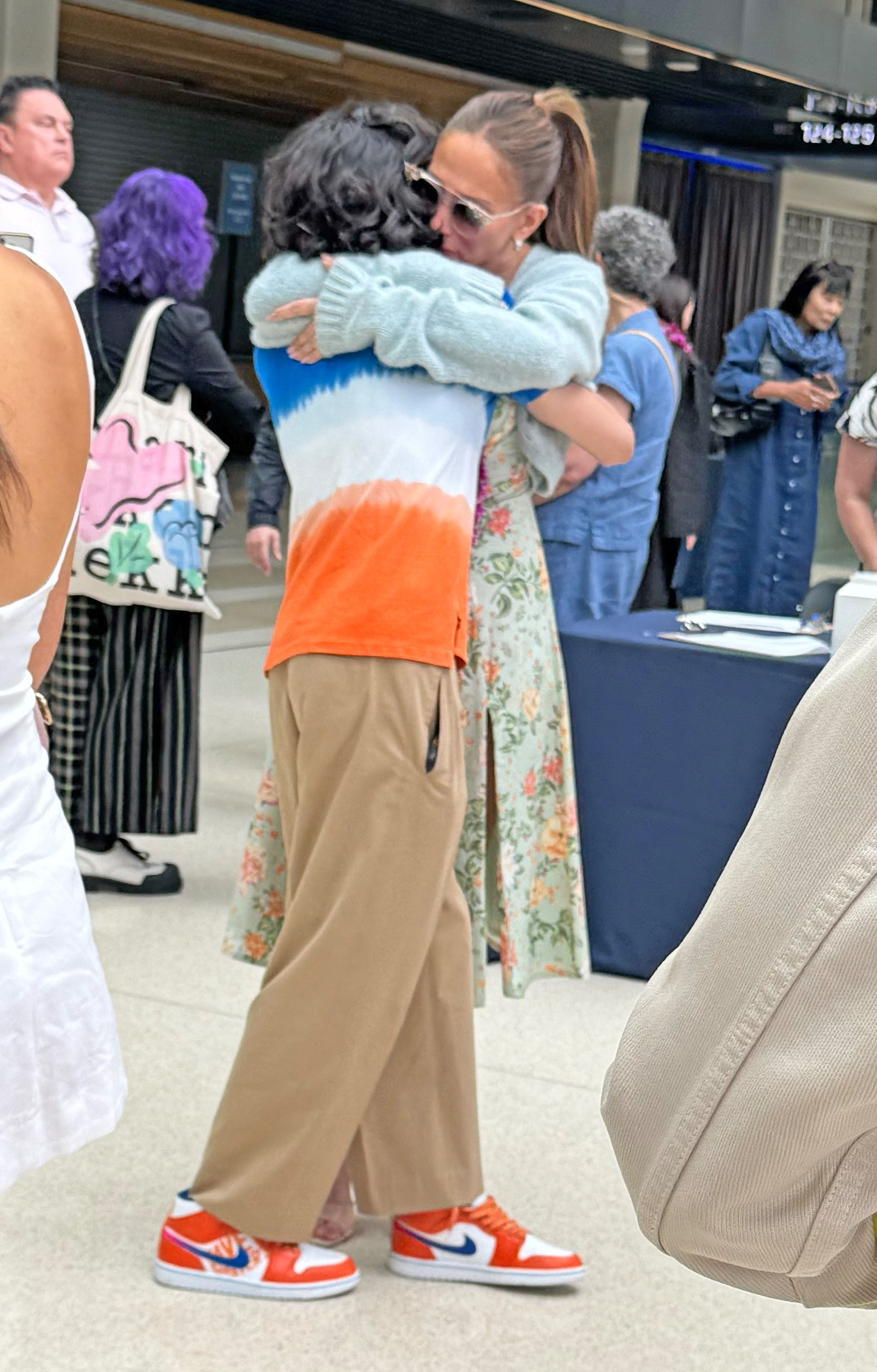 Jennifer Lopez, wearing a floral dress, smiles for a photo with a group of people, with one person holding a diploma.