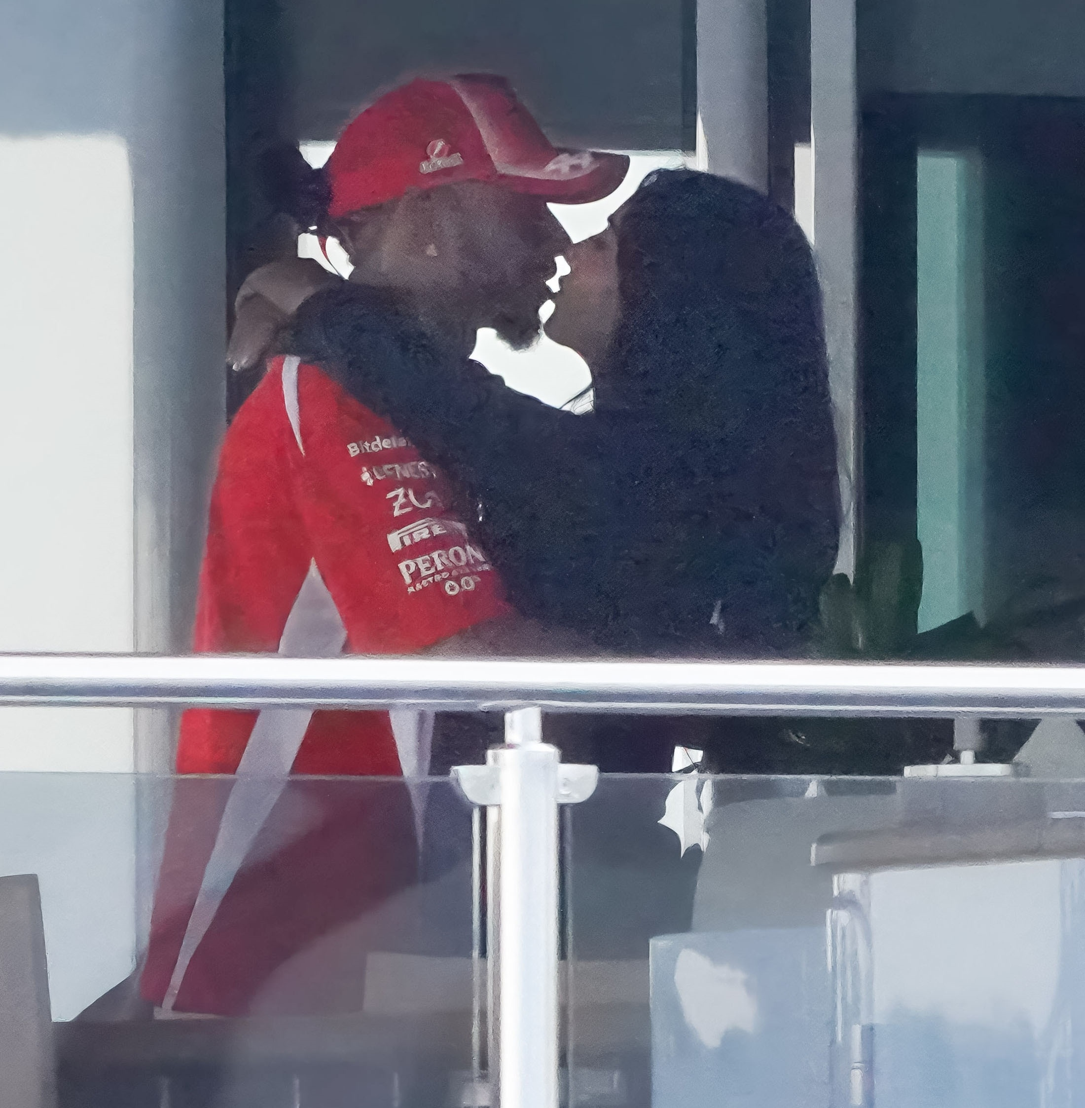 Kim Kardashian embracing and kissing Lewis Hamilton, who is wearing a red racing polo and cap, on a yacht.