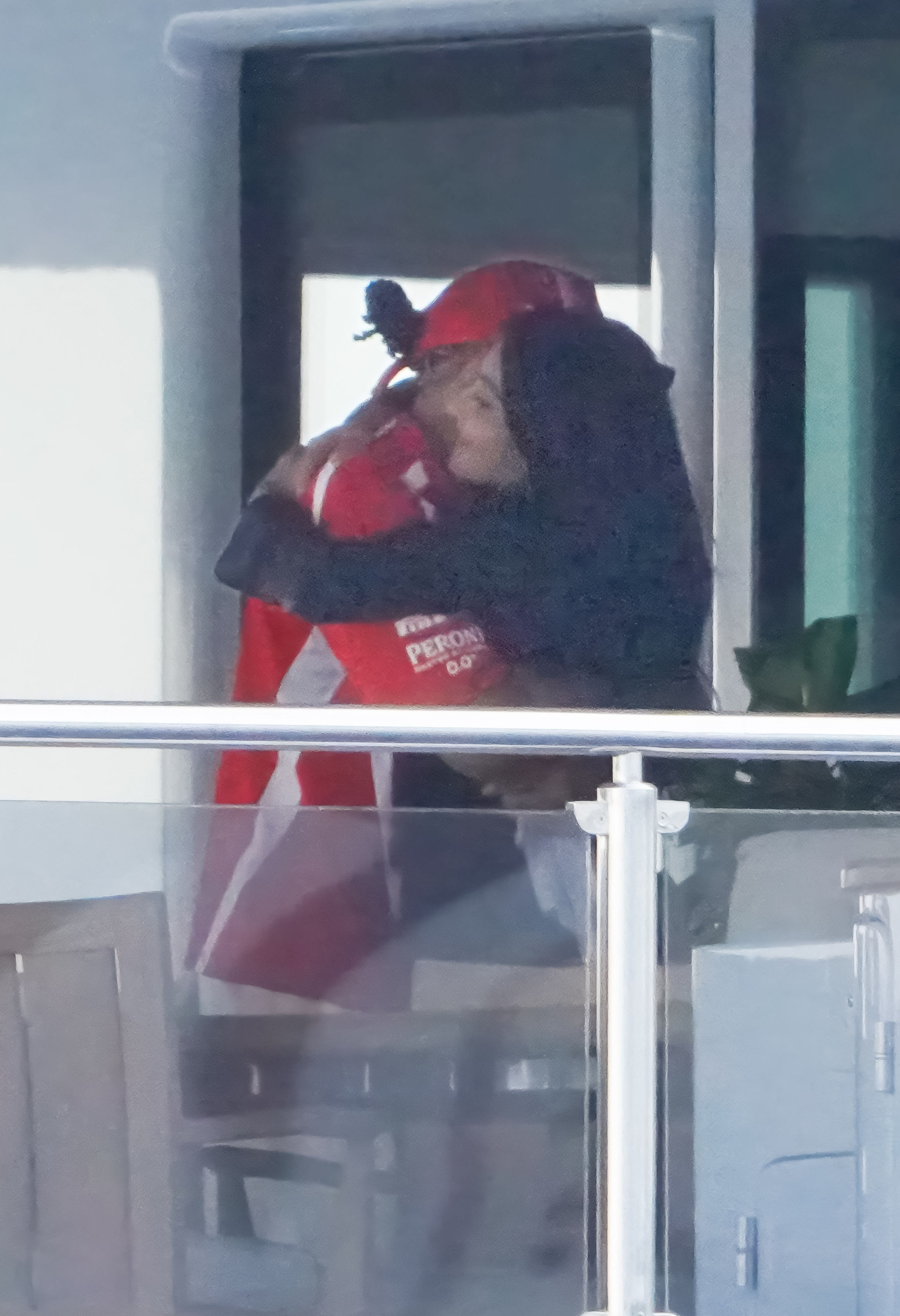 Kim Kardashian embracing Lewis Hamilton, who is wearing a red racing team polo shirt and red baseball cap.