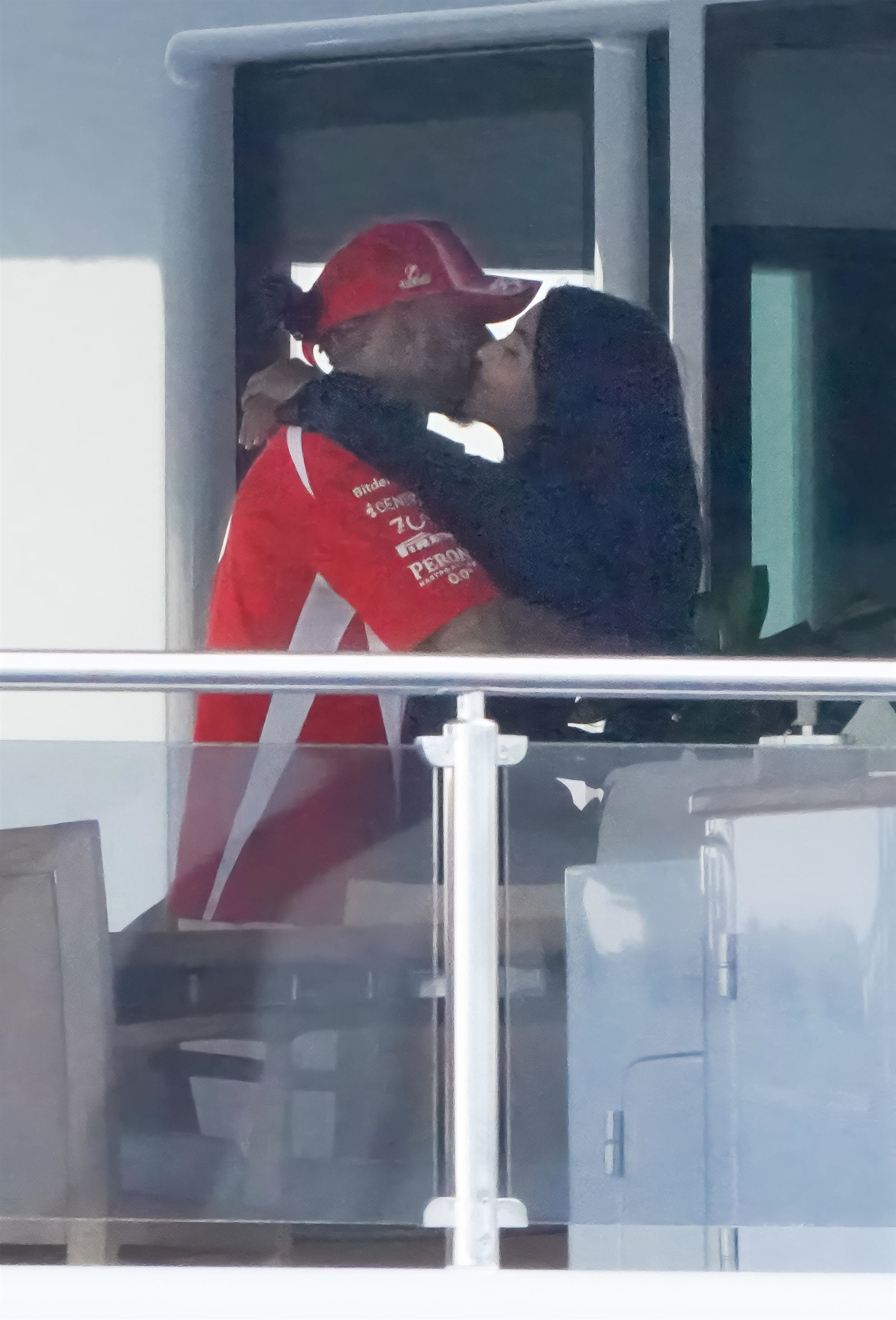 Lewis Hamilton, in a red racing polo and cap, embraces Kim Kardashian, in a long-sleeve black top, on a yacht.