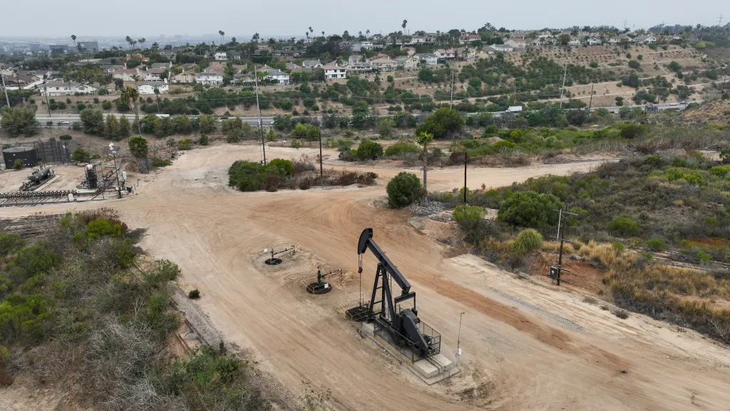 A drone's eye view of oil rigs in Baldwin Hills, Los Angeles, with houses and roads in the background.
