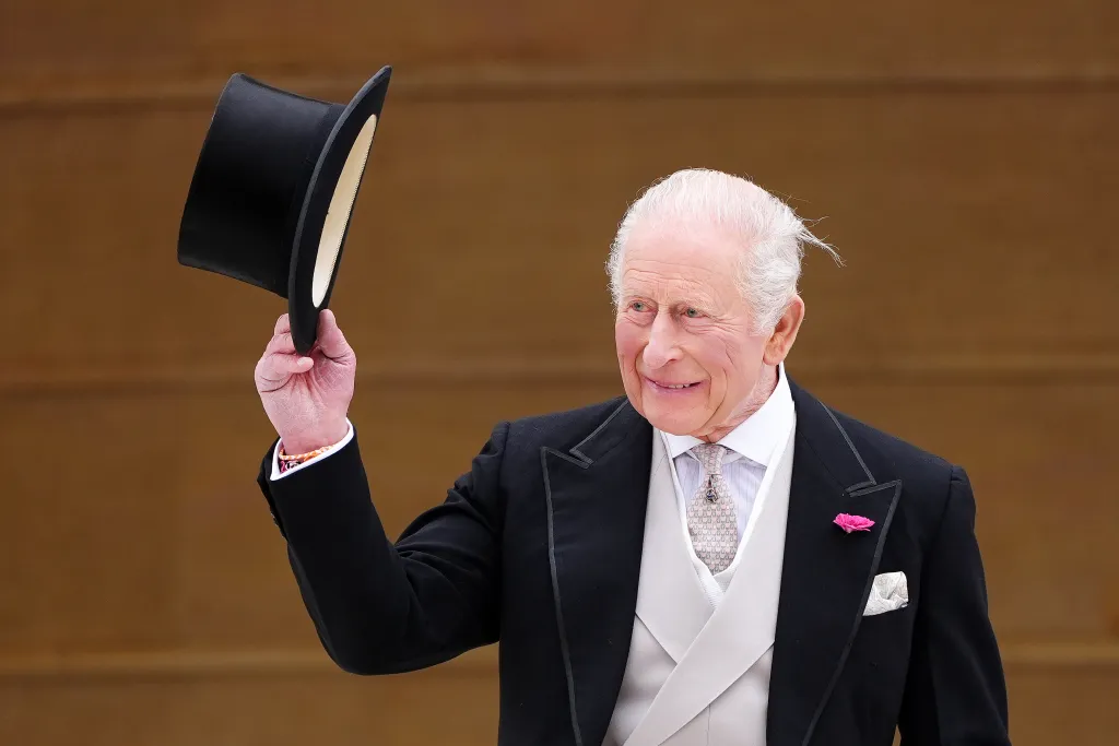 King Charles III in formal attire raising a top hat.