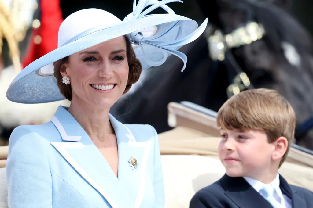 Catherine, Princess of Wales, in a light blue suit and matching hat, smiles next to Prince Louis in a carriage during Trooping The Colour.