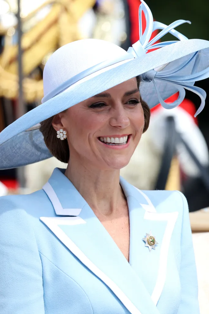 Catherine, Princess of Wales, smiles wearing a light blue hat and suit with a medal.