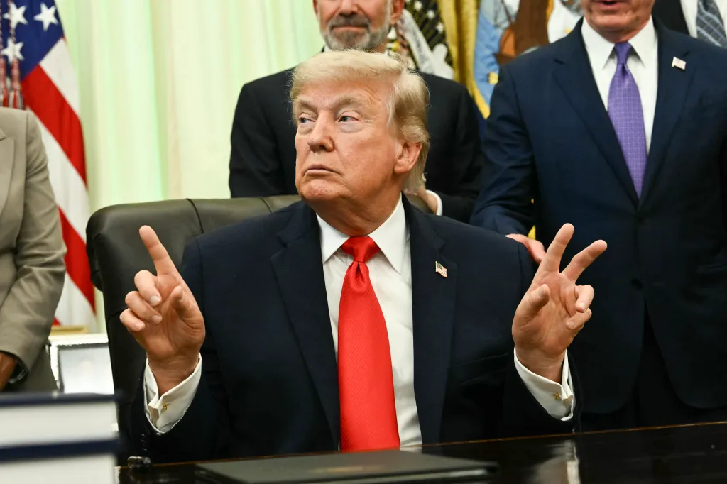 Donald Trump gesturing with both hands while seated at a desk.