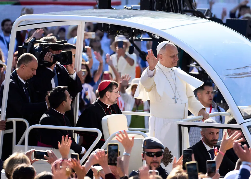 Pope Leo XIV waves to a crowd from his Popemobile.