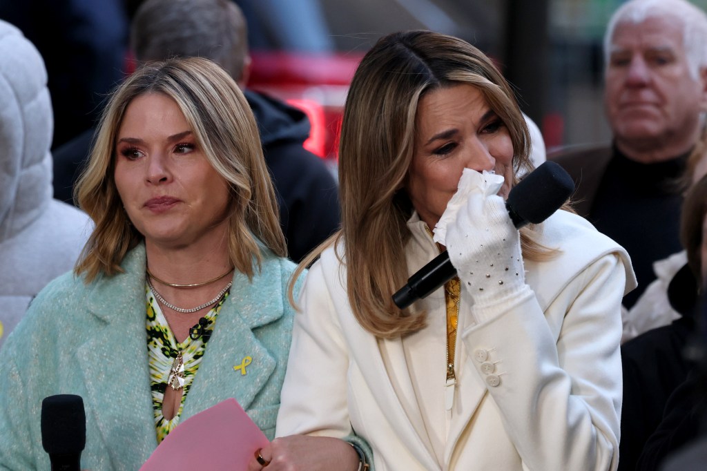 Savannah Guthrie, in a white coat and white gloves, wiping tears with a tissue while Jenna Bush Hager, in a green coat and green dress, looks on, both wearing microphones.