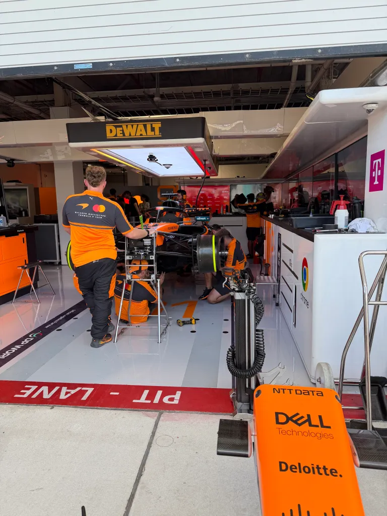 A Formula 1 pit lane with a car being serviced by crew members in orange uniforms.
