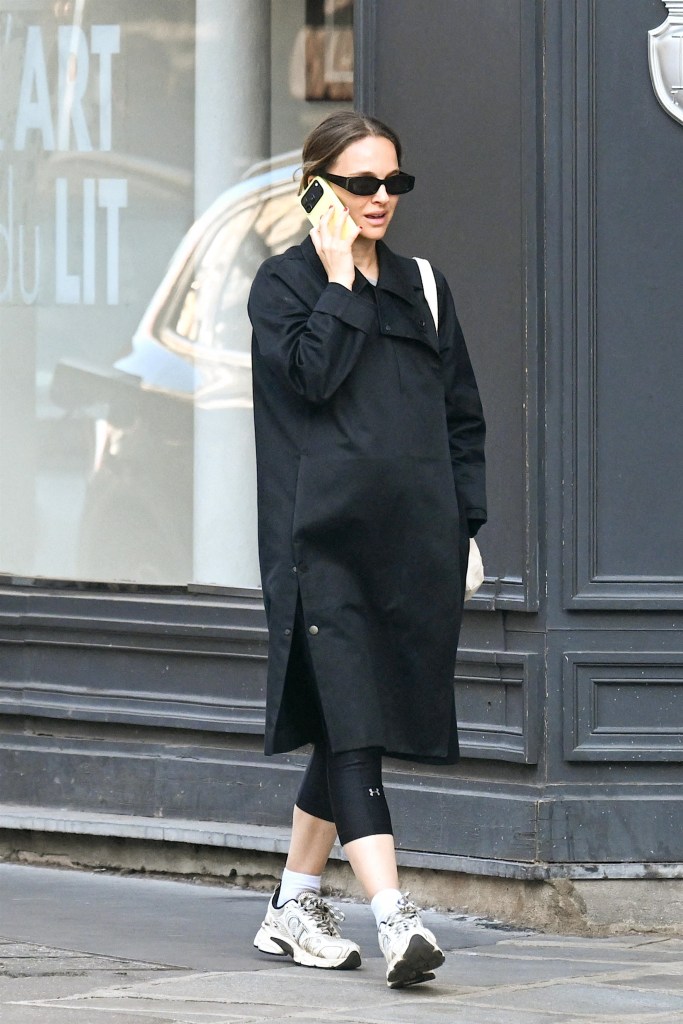 Natalie Portman wearing a black coat, black leggings, white sneakers, sunglasses, and talking on a neon green phone.