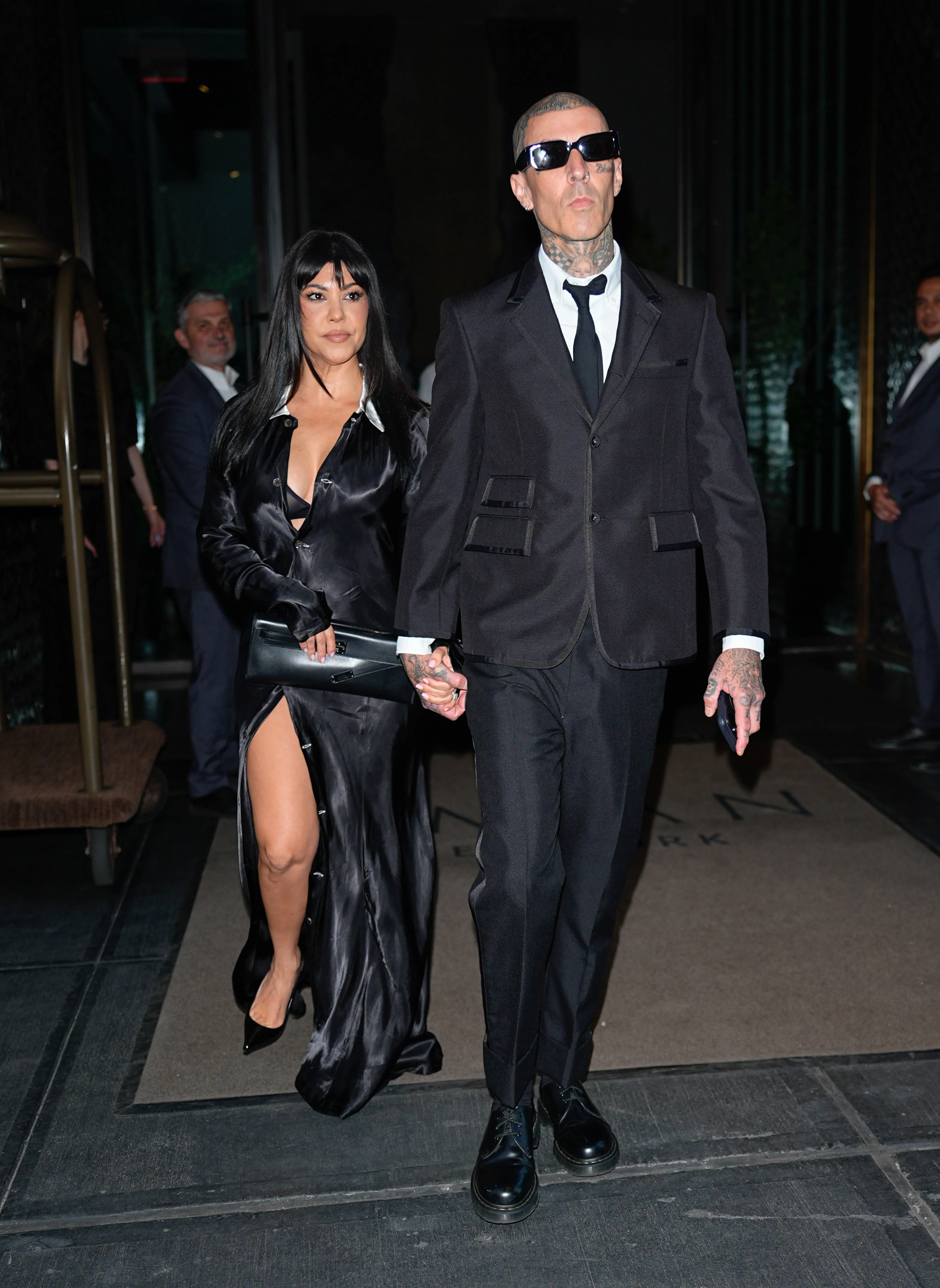 Kourtney Kardashian and Travis Barker holding hands, both dressed in black.