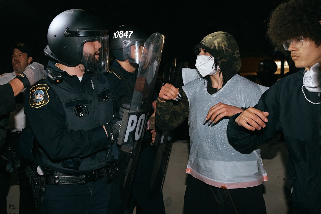 Protestors and police in riot gear clashing outside a detention facility.