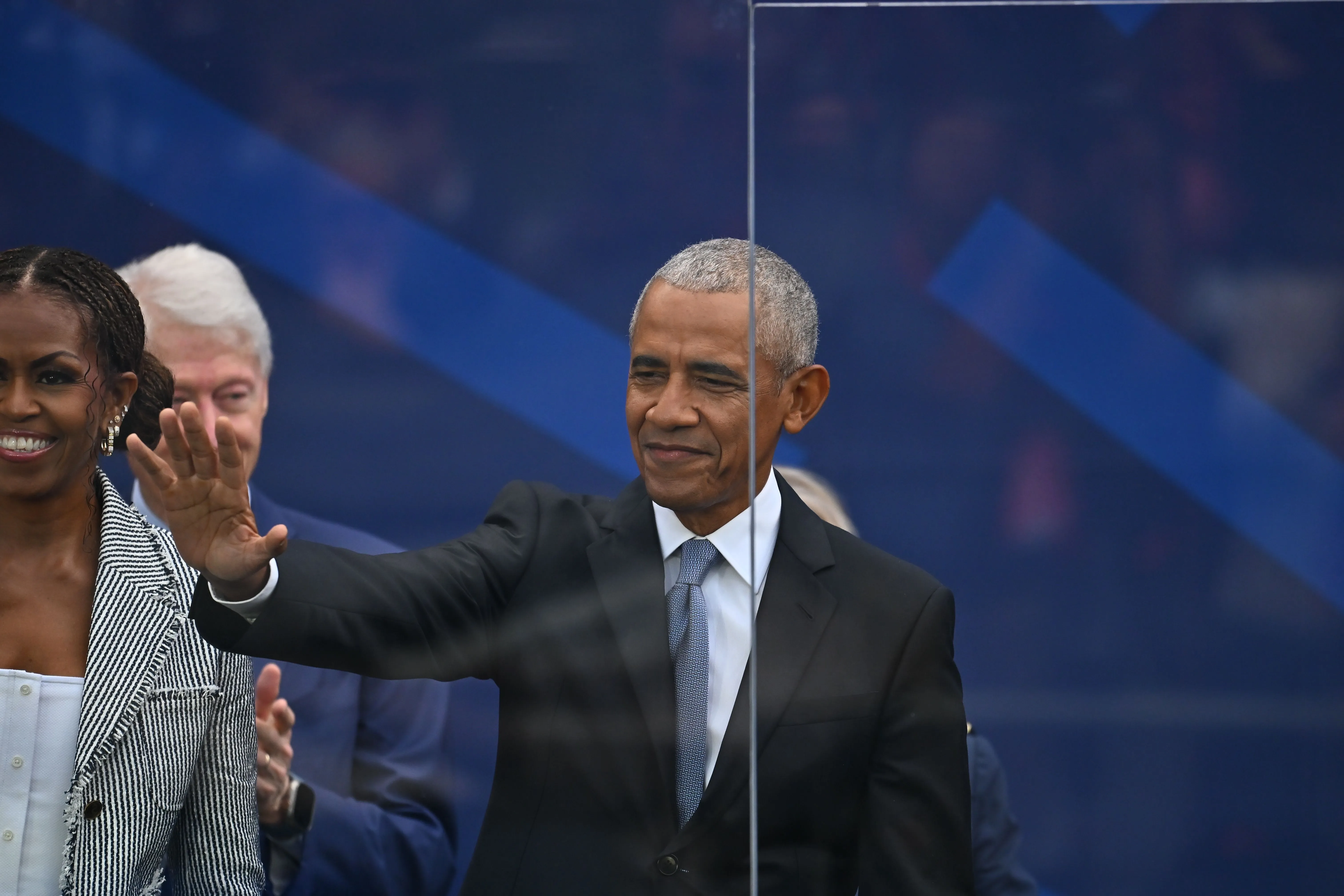 Barack Obama waves to a crowd with Michelle Obama and Bill Clinton behind him.
