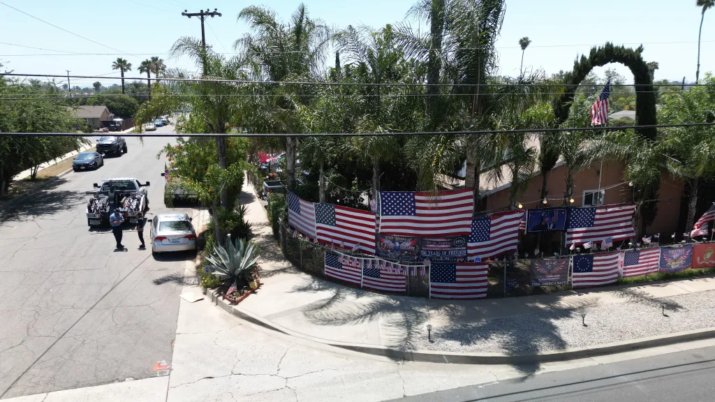 A residential street scene with a tow truck and car at the curb, and a house heavily decorated with American flags and 