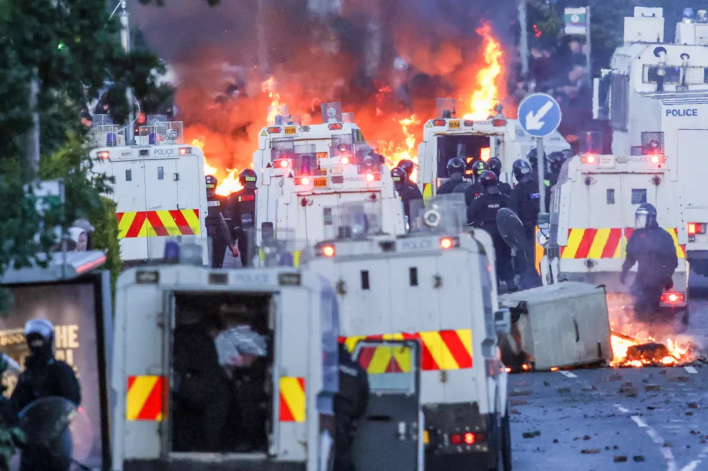 Police vehicles surrounded by fires and police officers in riot gear during unrest in Glengormley, Northern Ireland.