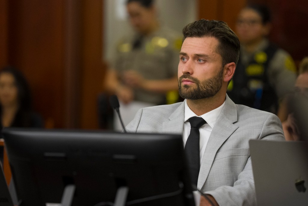 Dakota Mortensen sits in a courtroom wearing a light grey suit and black tie.
