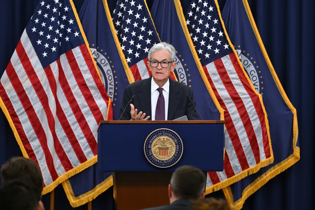 Jerome Powell, Federal Reserve Chair, speaking at a press conference with US and Federal Reserve flags behind him.