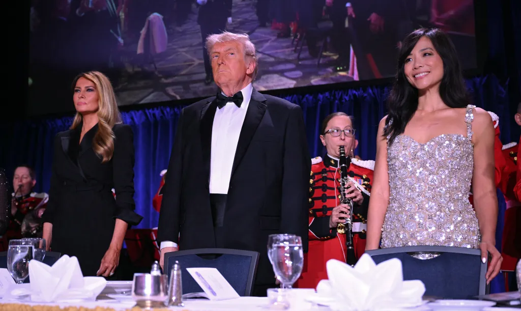 Melania Trump, Donald Trump, and Weijia Jiang stand behind a formal dinner table.