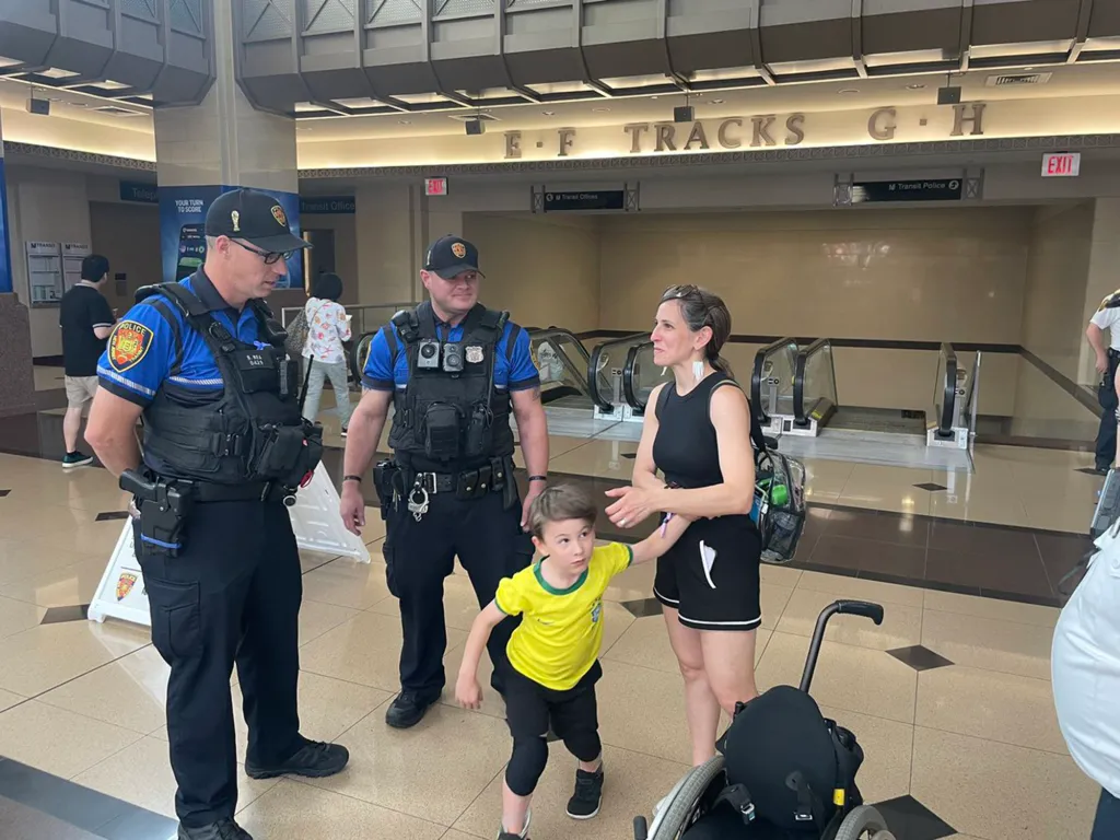 Two police officers, a woman, and a boy in a yellow shirt stand in a transit station.