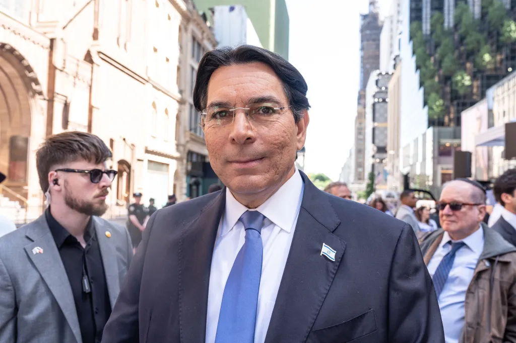 A man in a suit and tie, wearing an Israeli flag pin, stands in New York's Fifth Avenue.