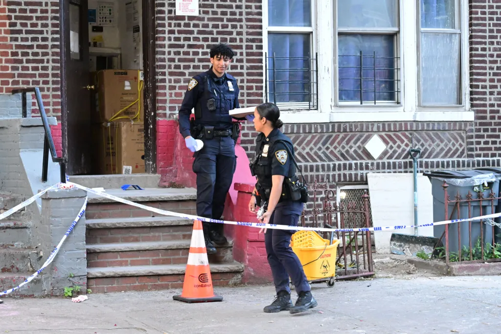 Two police officers standing on a sidewalk outside a building where a man was found dead, with crime scene tape visible.