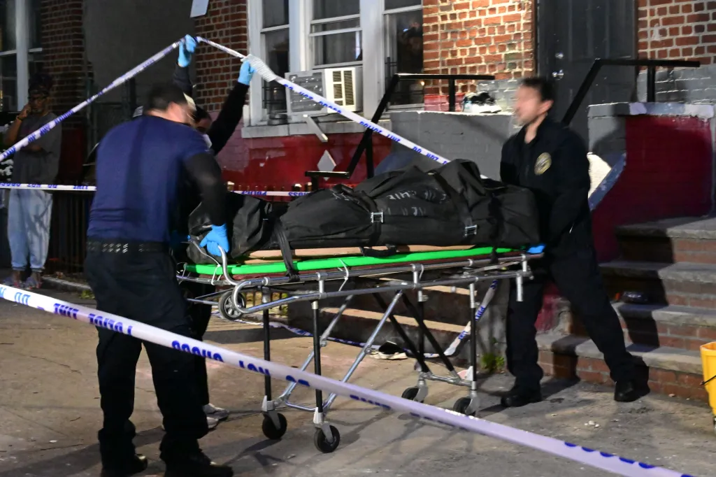 Law enforcement personnel moving a body bag on a gurney.
