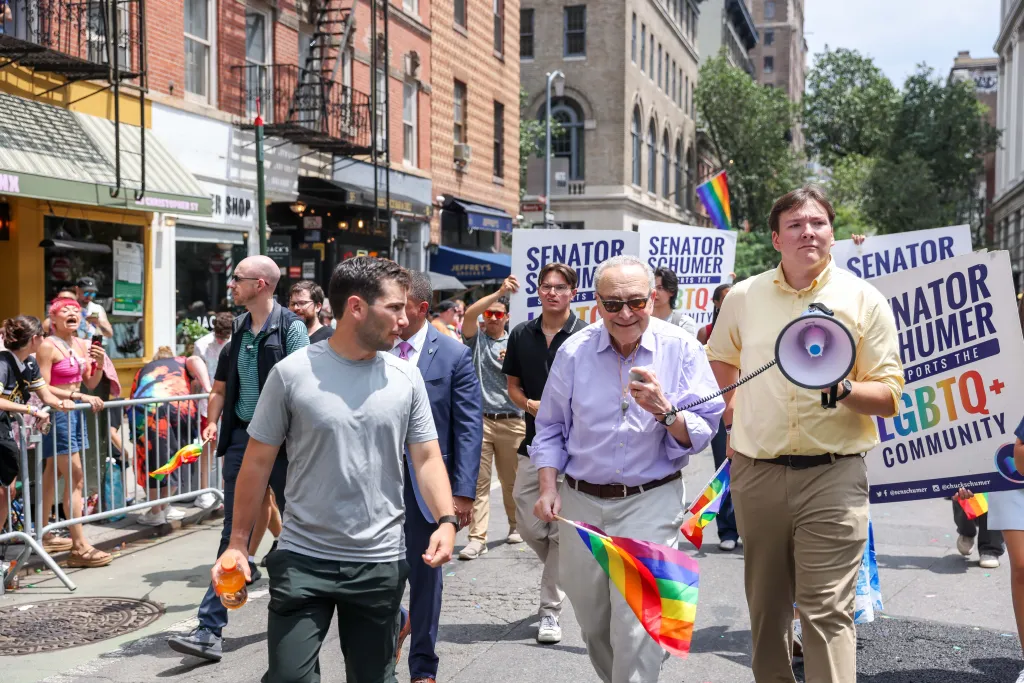 Senator Chuck Schumer marches in the NYC Pride March, holding a small rainbow flag.