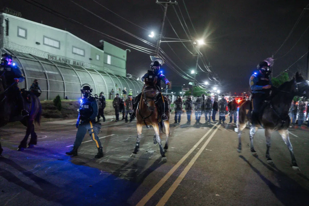 New Jersey State Police officers on horses and on foot clearing protesters in front of the Delaney Hall detention facility at night.