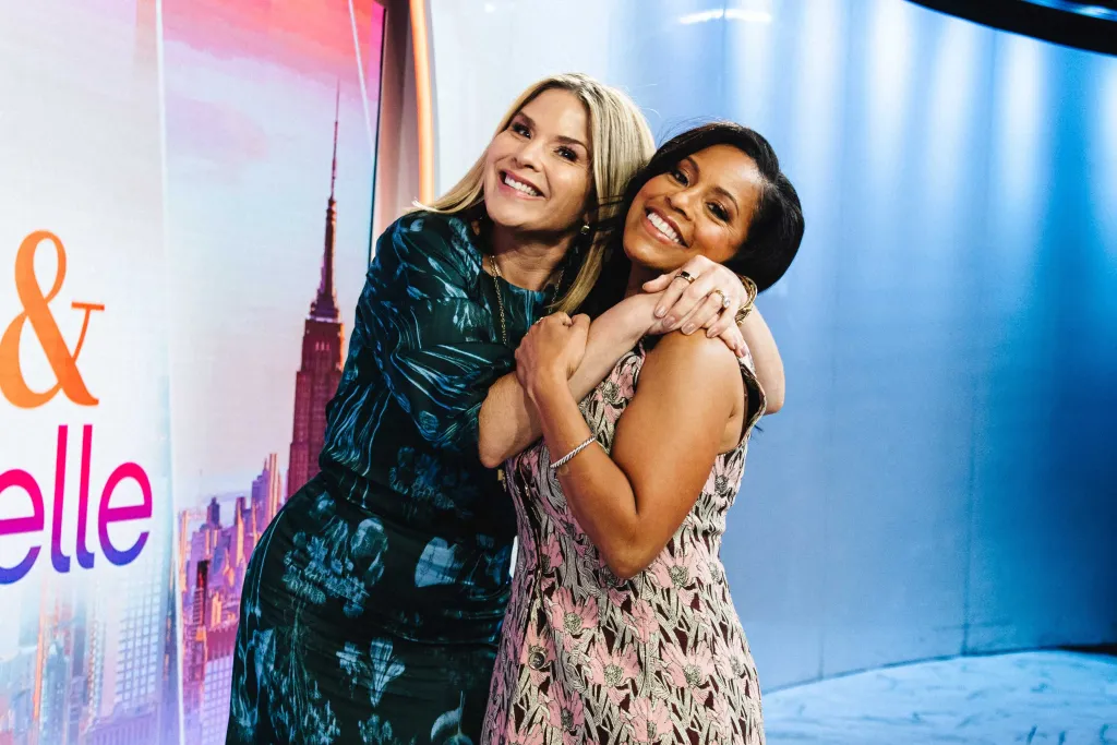 Jenna Bush Hager, in a black dress with blue print, and Sheinelle Jones, in a pink floral dress, smiling and embracing.