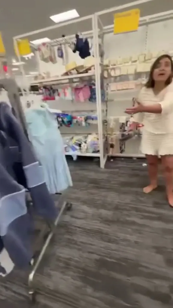 A barefoot woman in white shorts and top reacts to an incident in a store aisle.