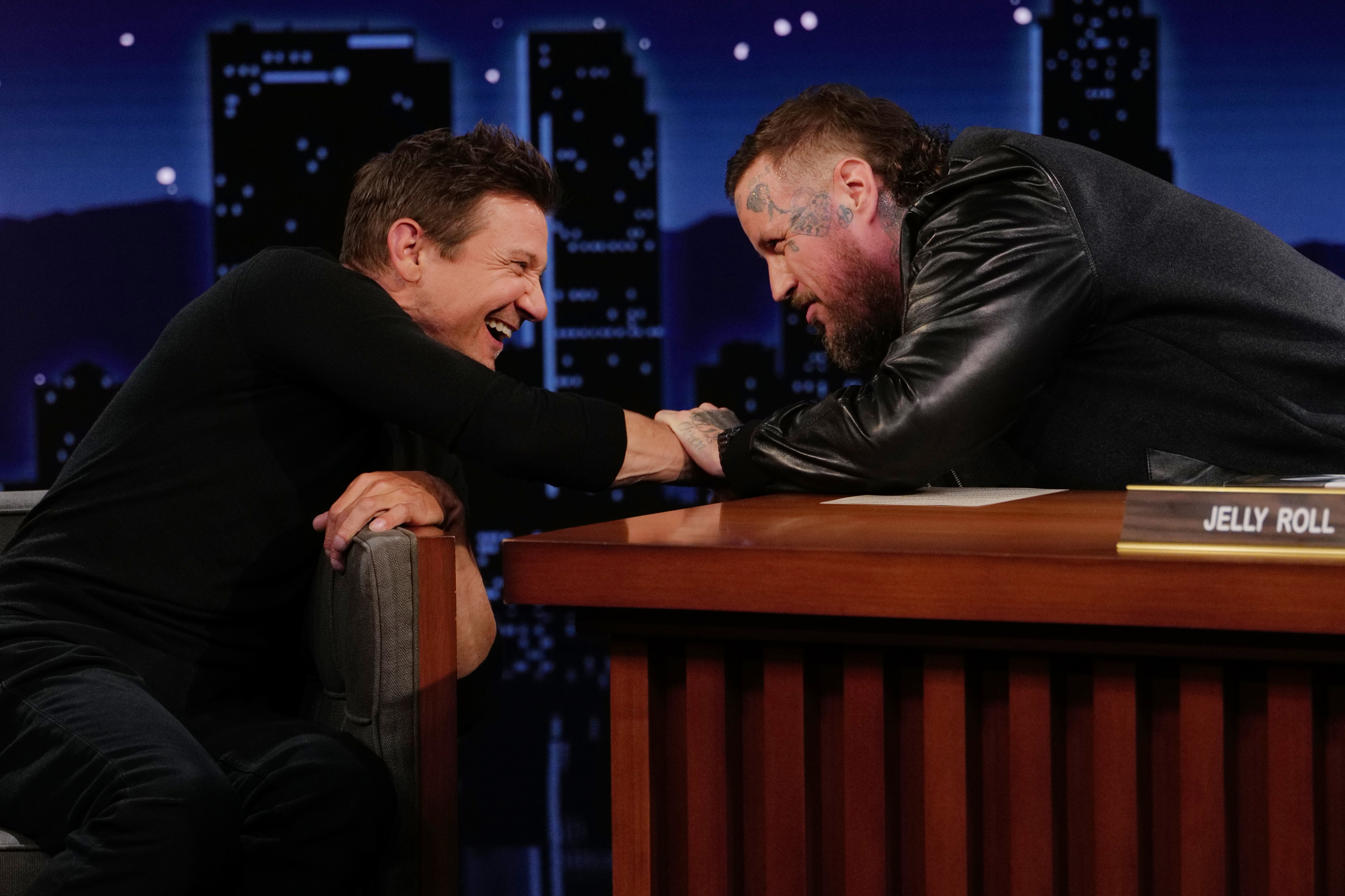 Jeremy Renner and Jelly Roll arm wrestling on a talk show.